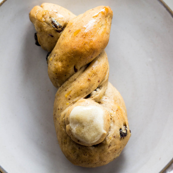 Close up of hot cross bun shaped like a bunny on a light gray plate. 