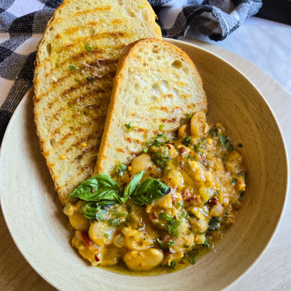 Golden grilled toast with a butter bean sauté garnished with green herbs and red pepper flakes.