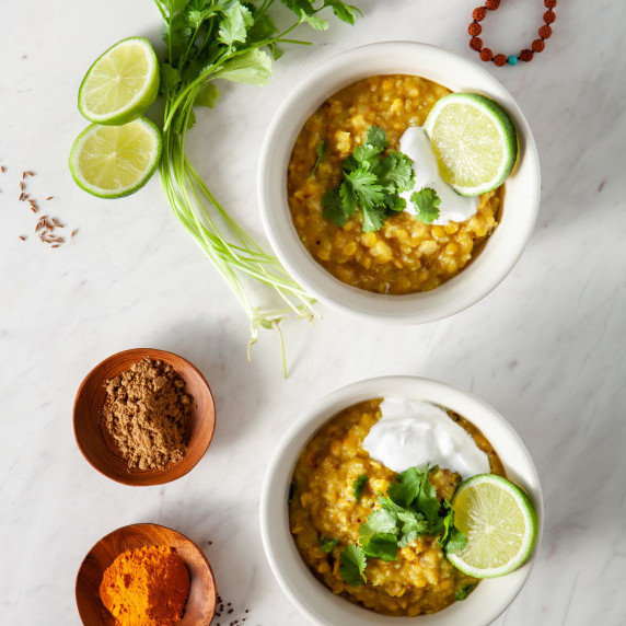 Two bowls of homemade kitchari topped with fresh herbs, yoghurt and lime