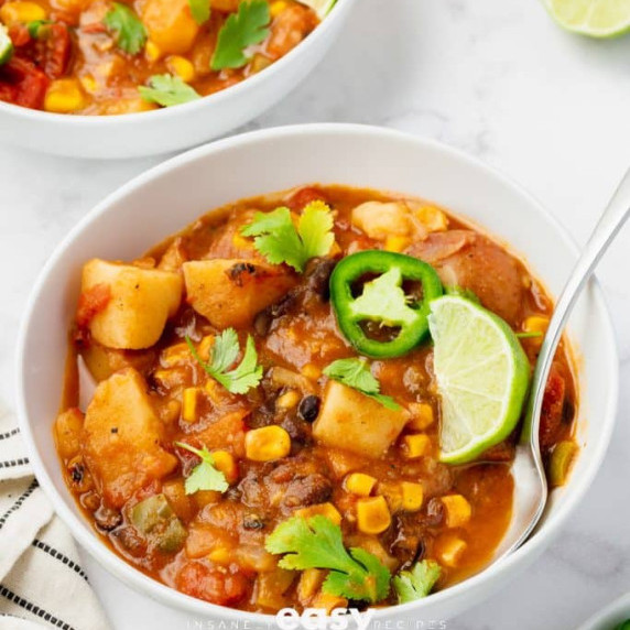 Vegan stew garnished with cilantro, jalapeno slice, and lime wedge on a white bowl with a spoon