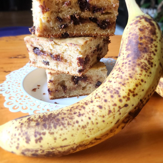 The image shows a delicious stack of baked goods with chunks of banana and chocolate on a white lace