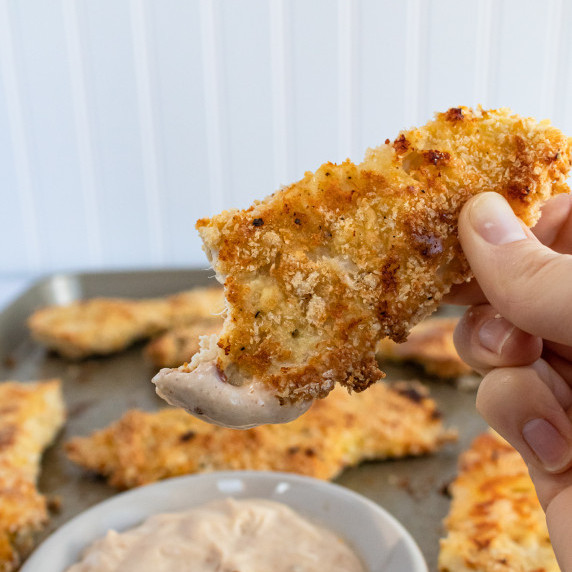 Baked Parmesan Chicken Tender being dipped in homemade sauce on a baking sheet