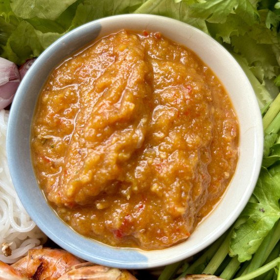 Top-view of Thai spicy peanut sauce with fresh vegetables, shrimp, and noodles.