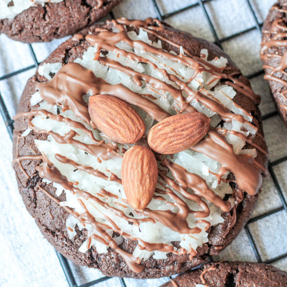 A chocolate cookie with a coconut topping, chocolate drizzle, and almonds on top