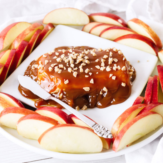 Caramel, toffee and cream cheese dip on a white square plate with a butter knife and apple slices