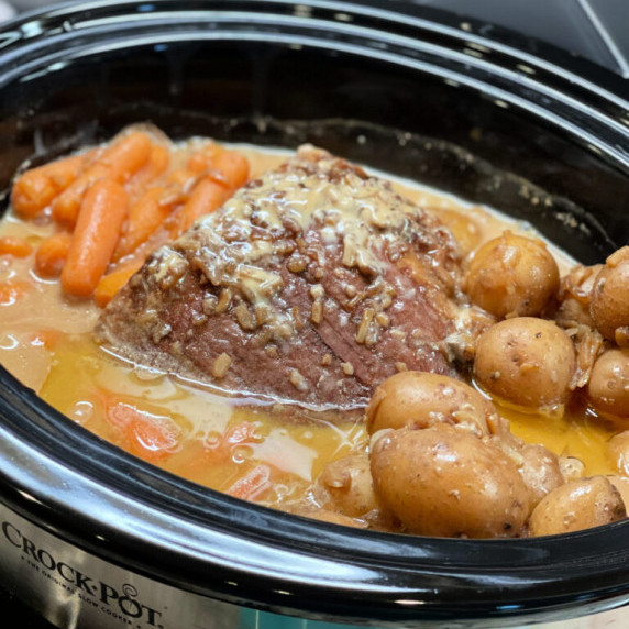 a slow cooker filled with roast, potatoes, and carrots