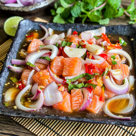 Close-up of Thai salmon salad with shallots, chilies, dressing, and green onions.