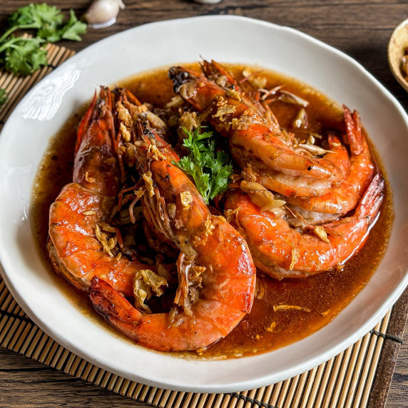 Close-up of Thai garlic shrimp with sauce in a white dish.