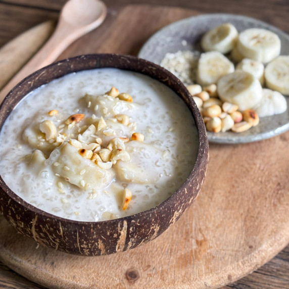 Vietnamese che chuoi, banana tapioca pudding, in a coconut shell with banana slices in the back.