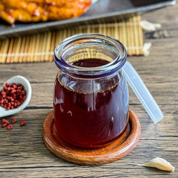 Inasal chicken oil in a glass cup with chicken behind.