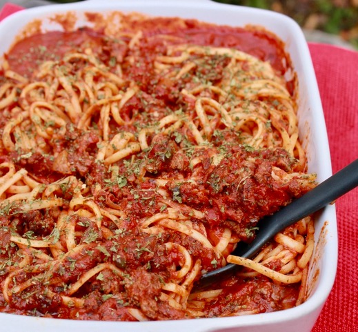 pasta in a white pan with a black spoon on a red tablecloth.
