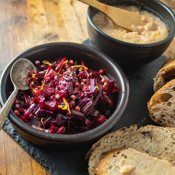 roasted beets stems in bowl with pink peppercorns and lemon zest on top. Toasted bread on side.