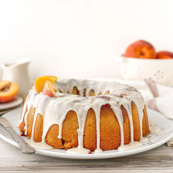 Peach Cobbler Pound Cake on a white serving plate with fresh peach slices on top.
