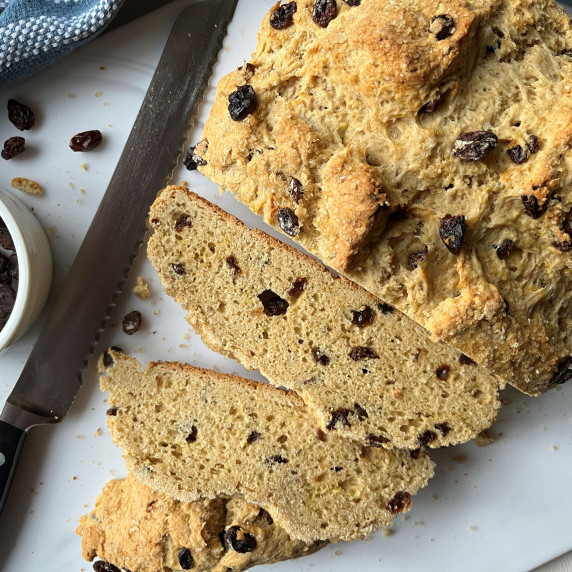 Sliced Irish Soda Bread on a marble cutting board with a serrated knife. 