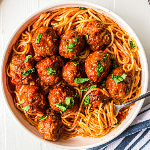 Meatballs in pasta sauce over top of spaghetti in a bowl.