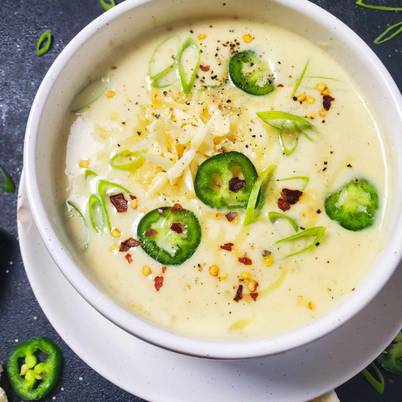 A creamy bowl of soup garnished with green and red against a black background.