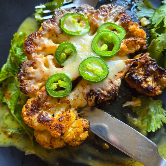 Slightly charred cauliflower steak with white cheddar, green jalapenos, and green garnishes 