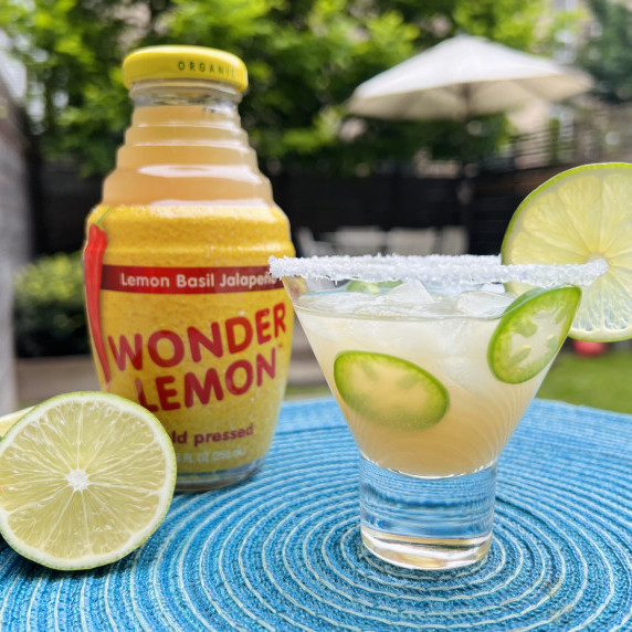 Drink with jalapeño slices and a lime wedge, on a blue placemat, w/ Wonder Lemon bottle behind