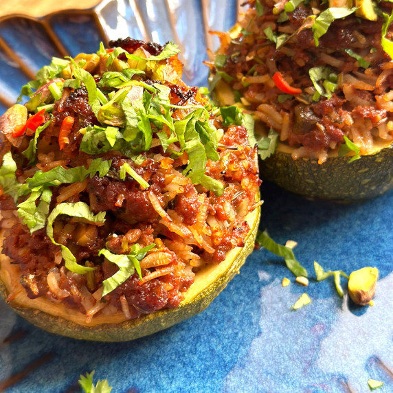 2 round zucchini dolmas stuffed with rice and mince mixture, topped with fresh herbs on a blue plate