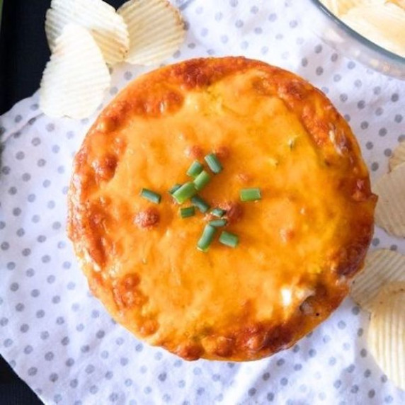 Loaded baked potato dip on a polka dot towel with chips scattered on the table.
