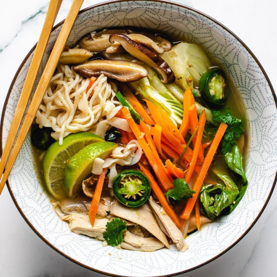 Turkey, peppers, carrots, lime, mushrooms and noodles in soup in a white bowl