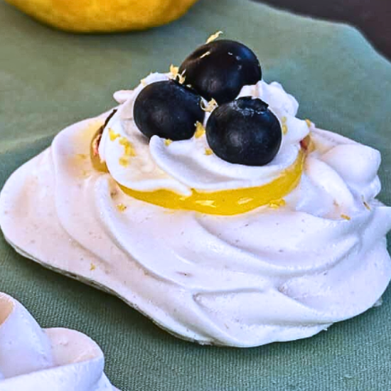 Mini Lemon Blueberry Pavlova topped with whipped cream, lemon curd, blueberries, and zest.