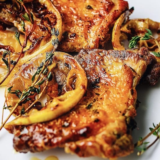 Chicken thighs, lemon slices and thyme sprigs on a white plate
