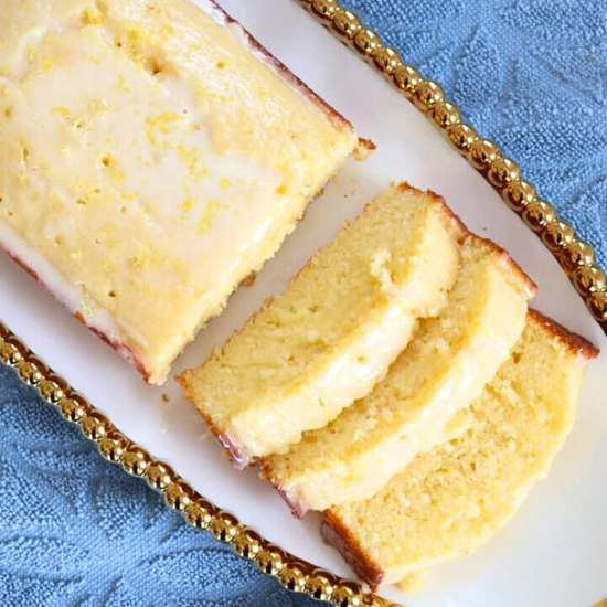 Lemon Loaf Cake with glaze, partially sliced, served on a white platter with gold trim.