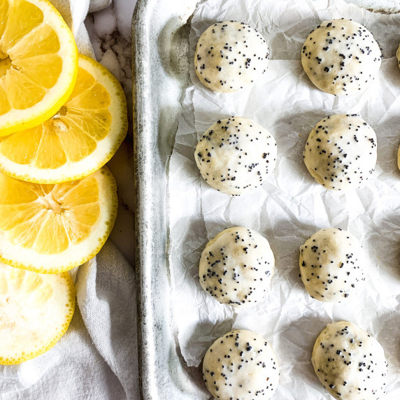 lemon poppyseed cookies on a cookie sheet next to sliced lemons