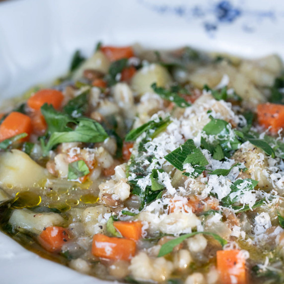 Overhead, close up photo, of lentil and barley soup, garnished with parmesan cheese and parsley.
