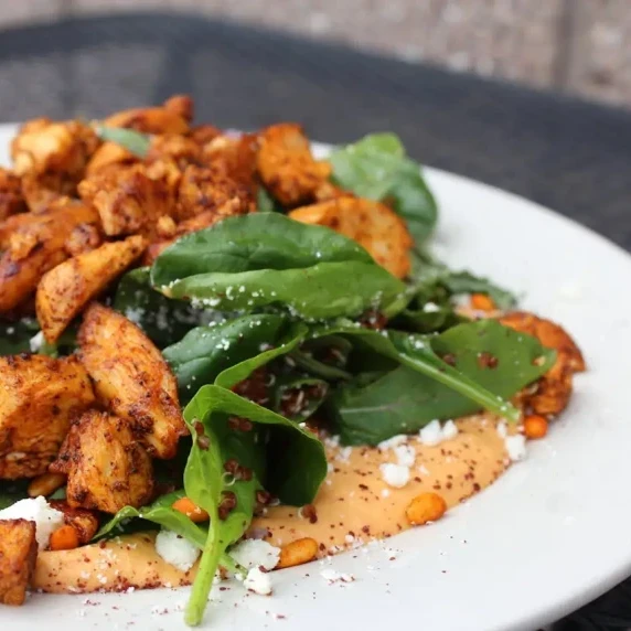 A plate of lightened-up Marry Me Chicken served with fresh spinach, a creamy sauce, and sprinkled ch