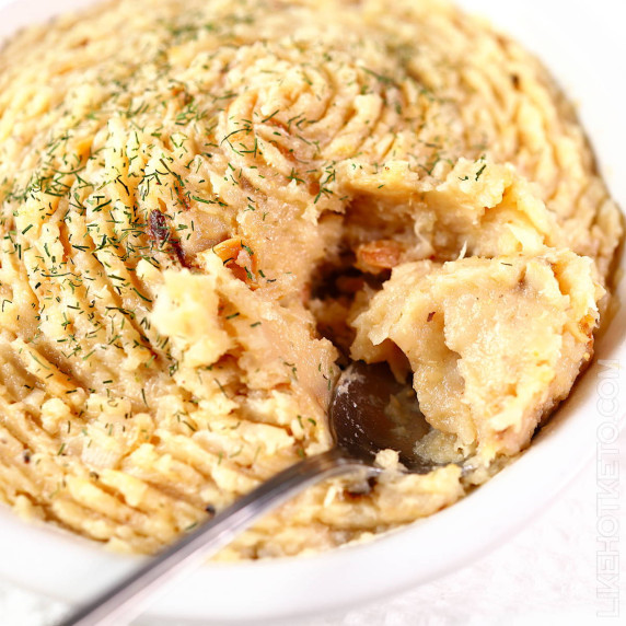 Golden and thick roasted turnip and garlic mash garnished with dill on a white plate, with a spoon.