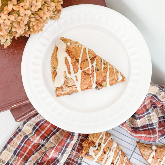 pumpkin spice scone on a white plate on a stack of books with others on a rack below