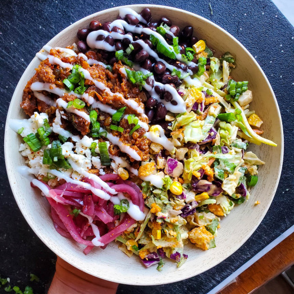A colourful, compartmentalized bowl of food in a wooden bowl against a black cutting board.