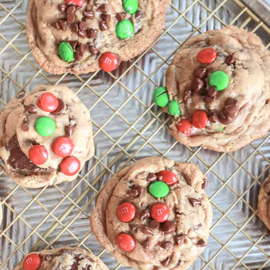 Chewy Christmas M&M and chocolate chip cookies cooling on a wire rack with red and green candies.