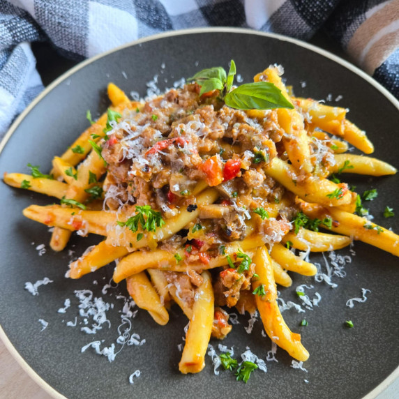 A plate of pasta topped with meat sauce and pops of green herbs against a checkered towel.