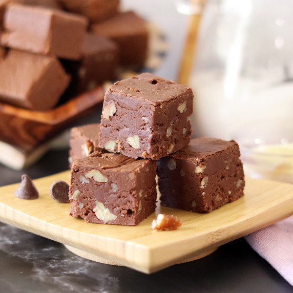 Several pieces of Mamie's fudge on a small wooden platter with more fudge in the background.