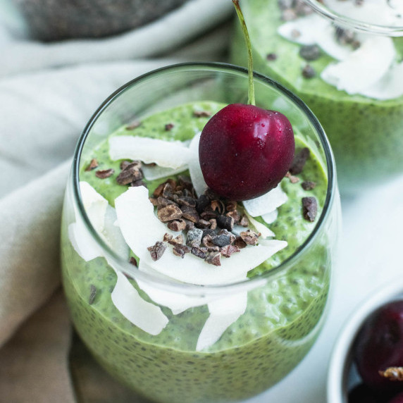 Two cups filled with chia pudding topped with coconut, cacao nibs, and sweet cherries.