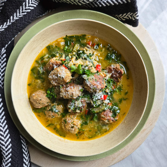 A bowl of meatball soup with pops of green & red against a black towel.