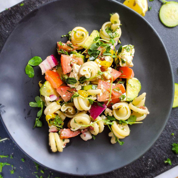 A colourful assortment of vegetables and pasta on a black plate with a black background