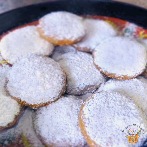 Mexican Tea Cakes with pecan and hazelnut dusted in powdered sugar on a brown and black plate