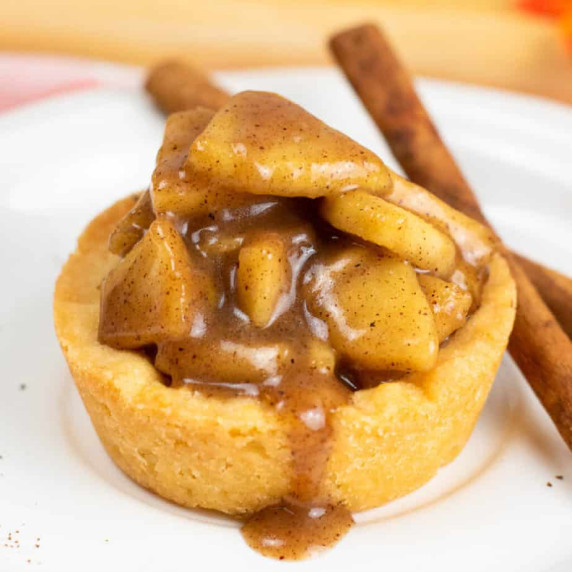 Close up side view of a sugar cookie cup filled with a gooey apple filling with some drizzling out.