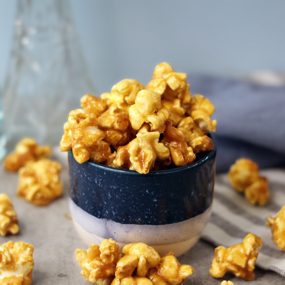 Caramel corn piled in a small bowl with more scattered on the table