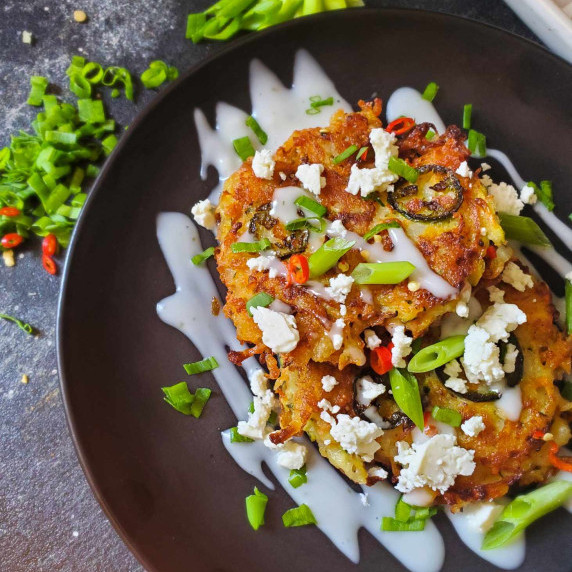 Crispy, golden vegetable pancakes, drizzled with white sour cream, feta crumbles, and herbs.