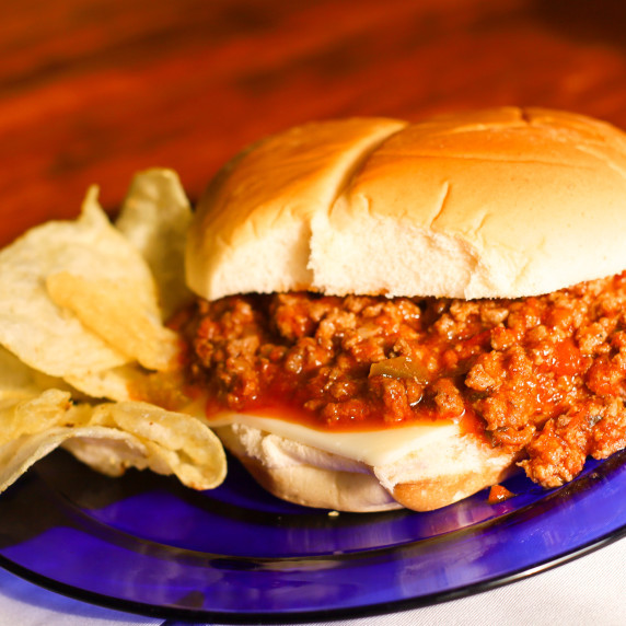 Sloppy Joe Sandwich with a side of potato chips on a blue plate