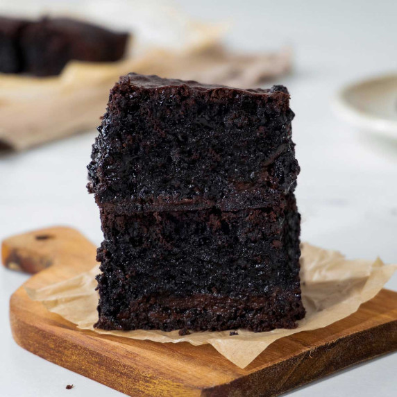 Two chocolate olive oil brownies stacked on a wooden board.