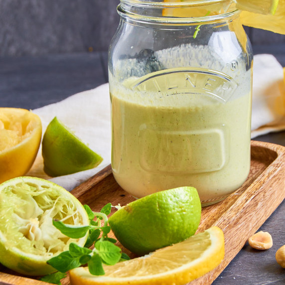 A jar of Orange Maple Vinaigrette with Hazelnuts and Lime on a small wooden tray. 