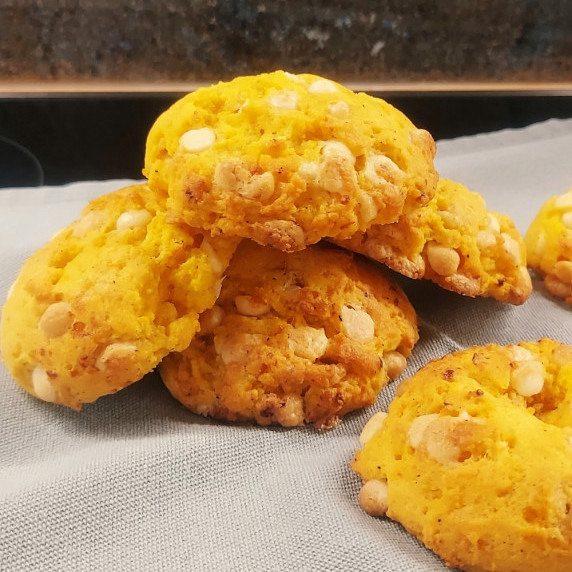 Chewy orange cookies with cream cheese baking chips, glowing with a sunny citrus hue.