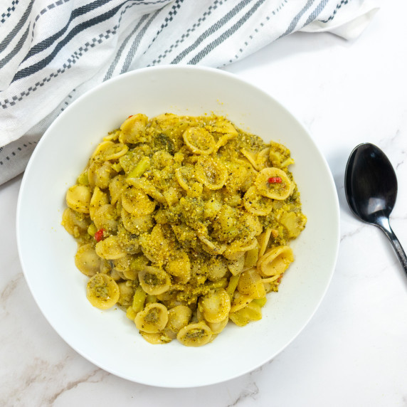 Top down shot of Orecchiette Con Broccoli flanked by a tea towel and a spoon for decoration. 