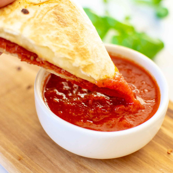 Pizza tortilla wrap being dipped in marinara sauce